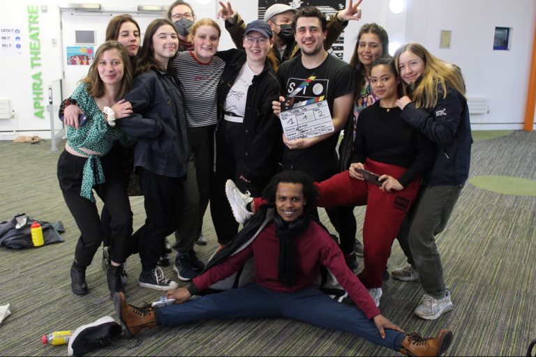 A group of students standing closely together facing the camera holding a clapper board.