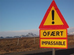 Photograph of a bright yellow road sign in Iceland that reads "! OFAERT Impassable"
