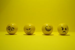 Image of four yellow balls each with a different facial expression painted on: worried, cheeky (sticking tongue out), happy (wide smile), and annoyed (downturned mouth, one frowning eye).