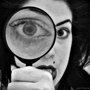 Photograph of a woman looking through a magnifying glass. One eye is enlarged as a result.