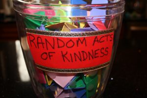 Photograph of a jar filled with coloured pieces of folded paper. Each piece contains an idea for a kind act.