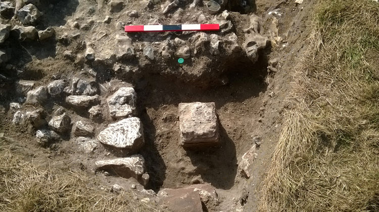Photo showing the corner with the added room (with chalk foundations) next to the earlier flint wall, with a stack of mortared tiles revealed, part of the pilae arrangmnet for the underfloor hypocaust.