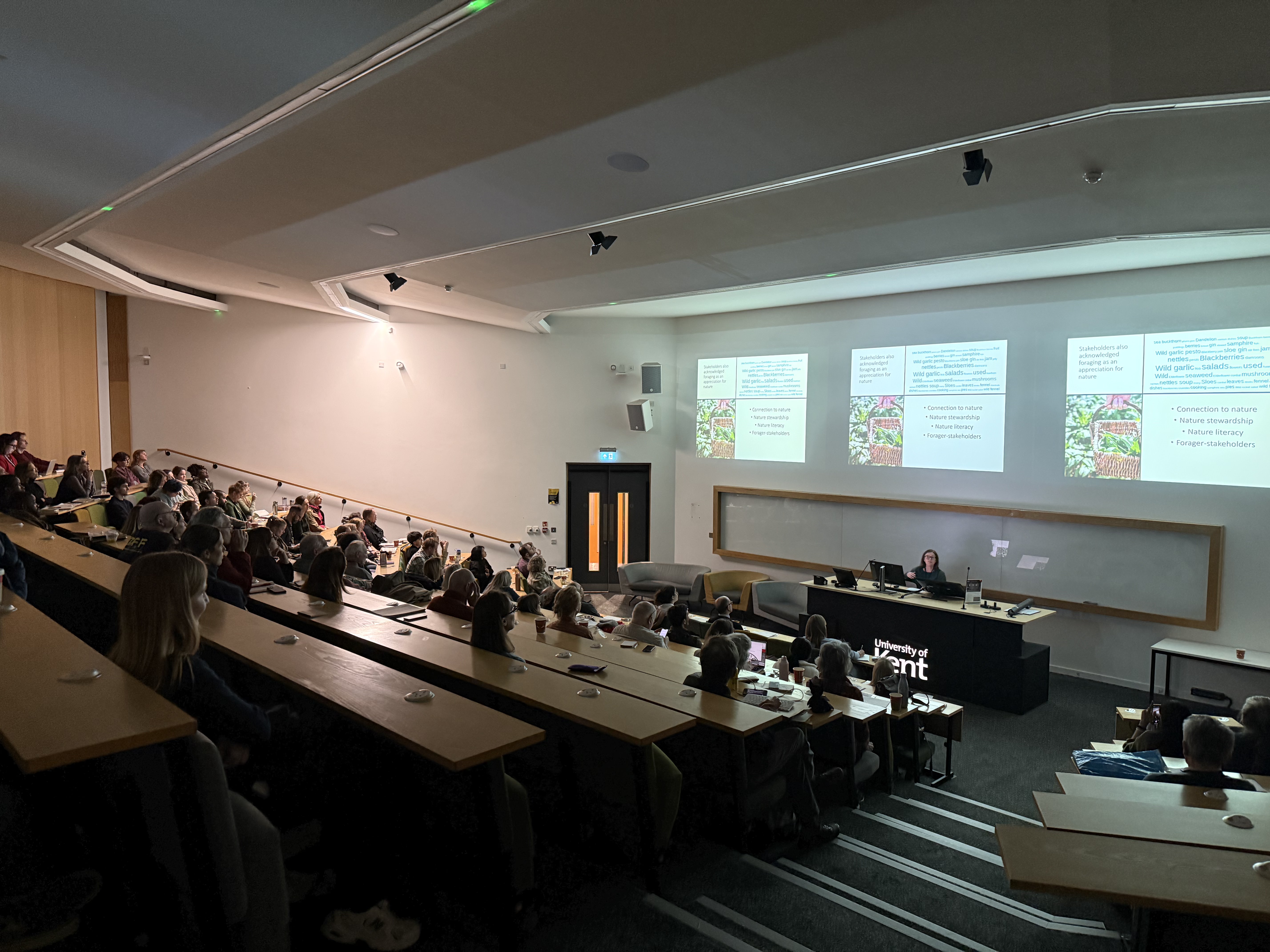 A woman stands at a lecturn presenting to an audience