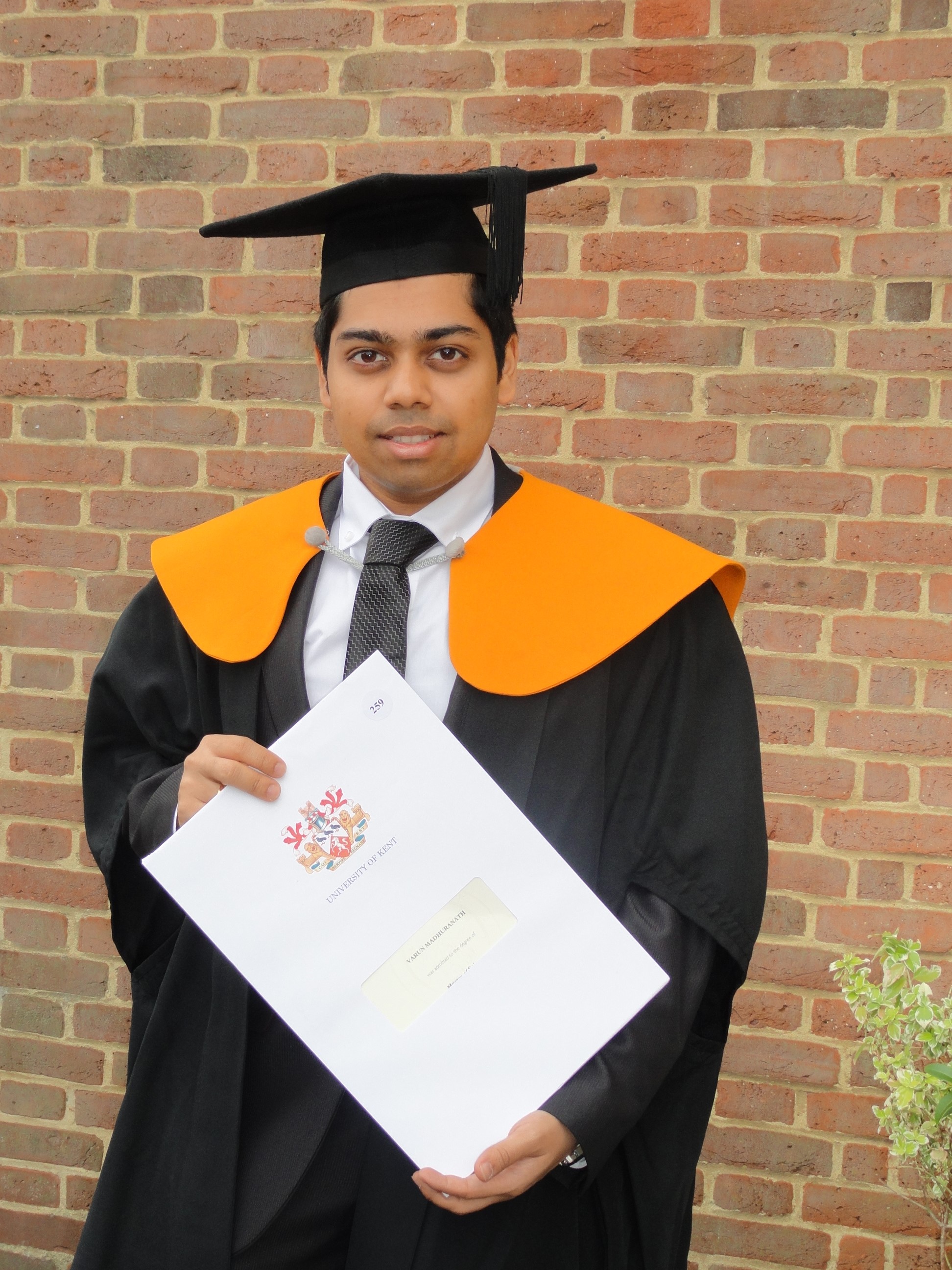 Varun holding his graduation degree certificate in his gown
