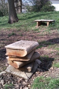 A pile of carved wooden books and a bench at an outside meeting place on the University of Kent campus