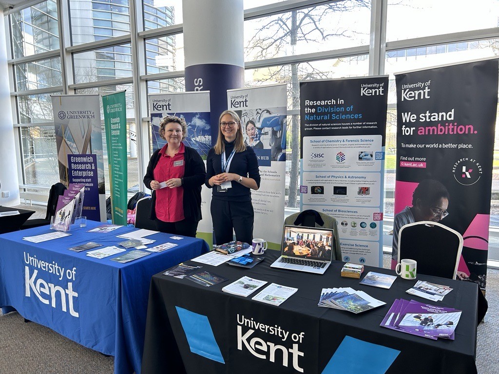 Two University of Kent staff smiling behind a branded Kent stand at the Discovery Park