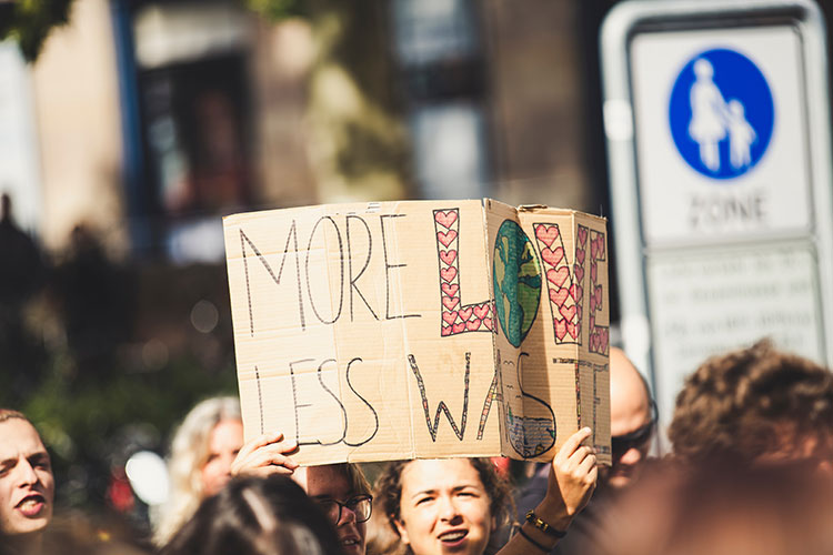 Girl holding a placard reading 'More Love, Less Waste'
