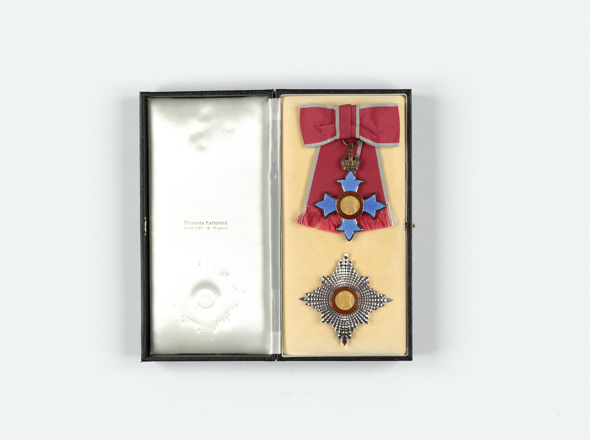 DBE medal in a boz with silk lining. The medal has a red and grey ribbon, a blue star, and a silver star emblem 