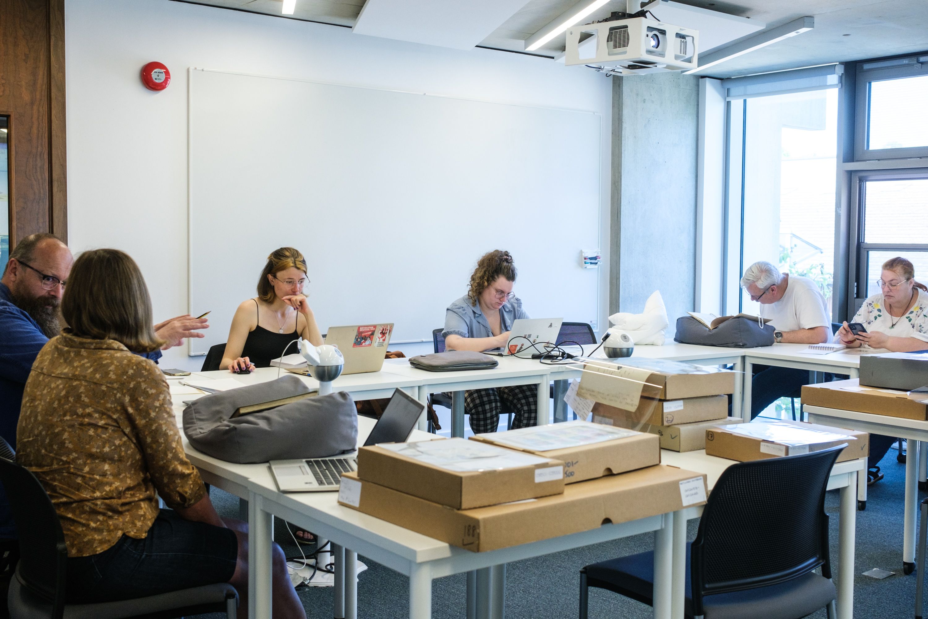 A room including six people sitting at tables looking at archive material 