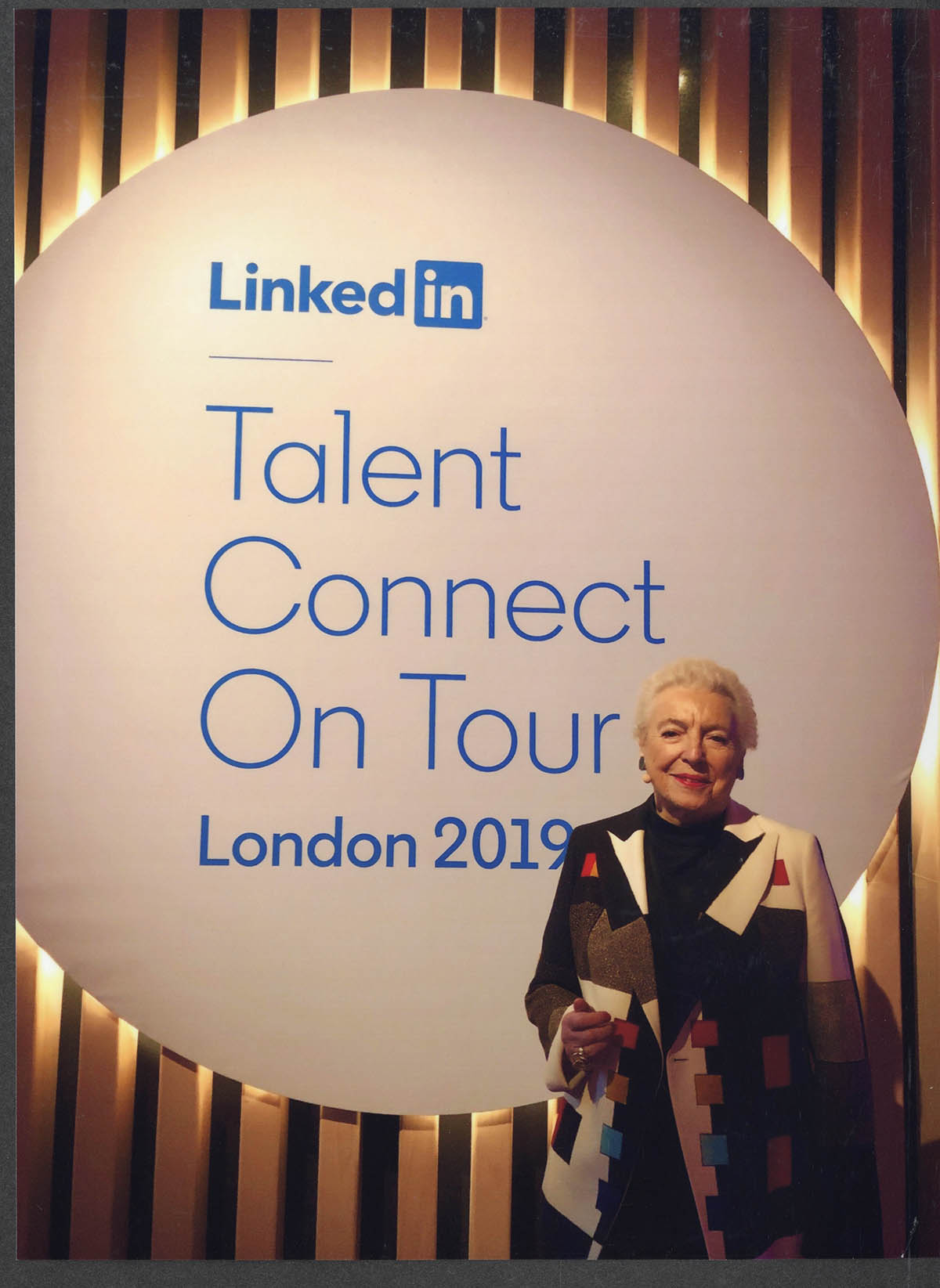 A photograph of Dame Stephanie Shirley standing in front of a large promotional sign at the 2019 Linkedin Summit, Talent Connect On Tour. 