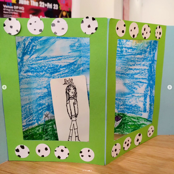 A hand-made pop-up book, showing a character in a landscape, with a decorative frame.