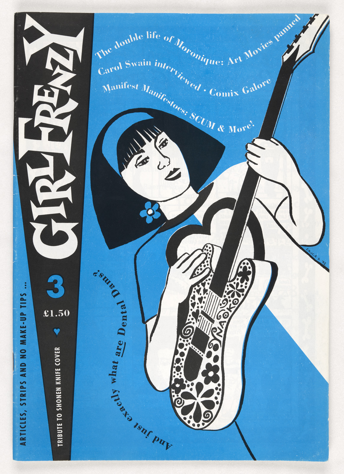 A photograph of the cover of GirlFrenzy zinie, blue cover with a drawn image of a woman playing a guitar