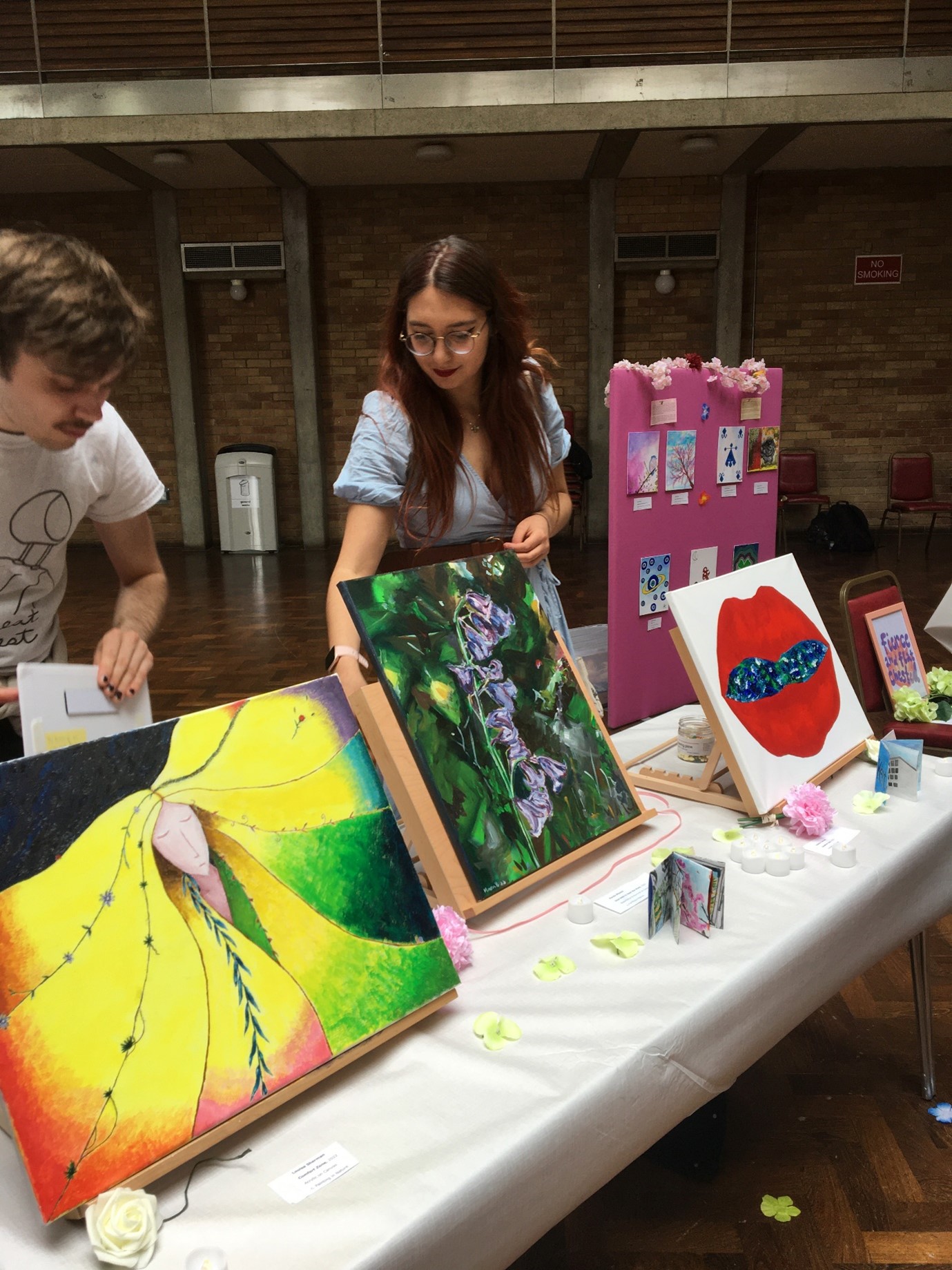 Two students arranging their artworks on tables.