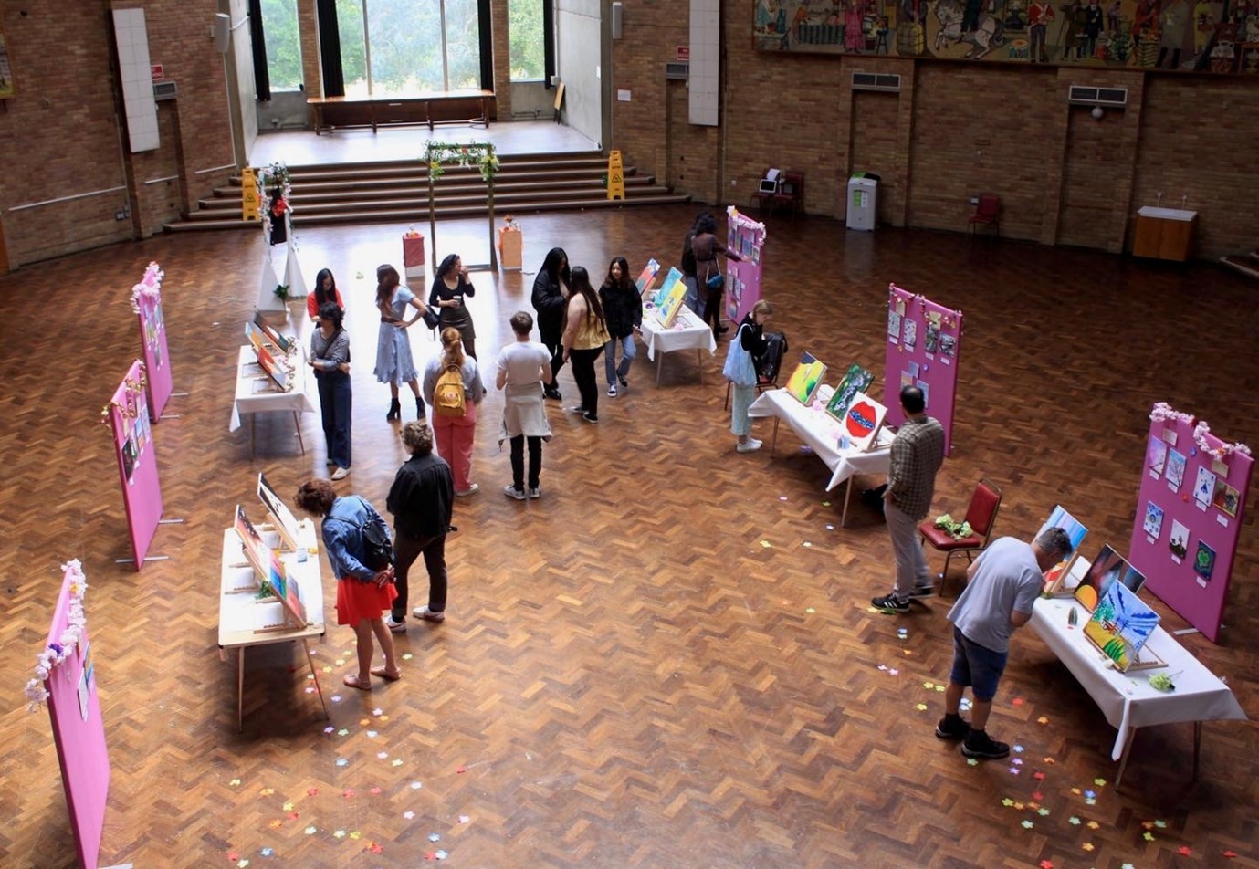 Wide-view photo of art exhibition in a hall with visitors.