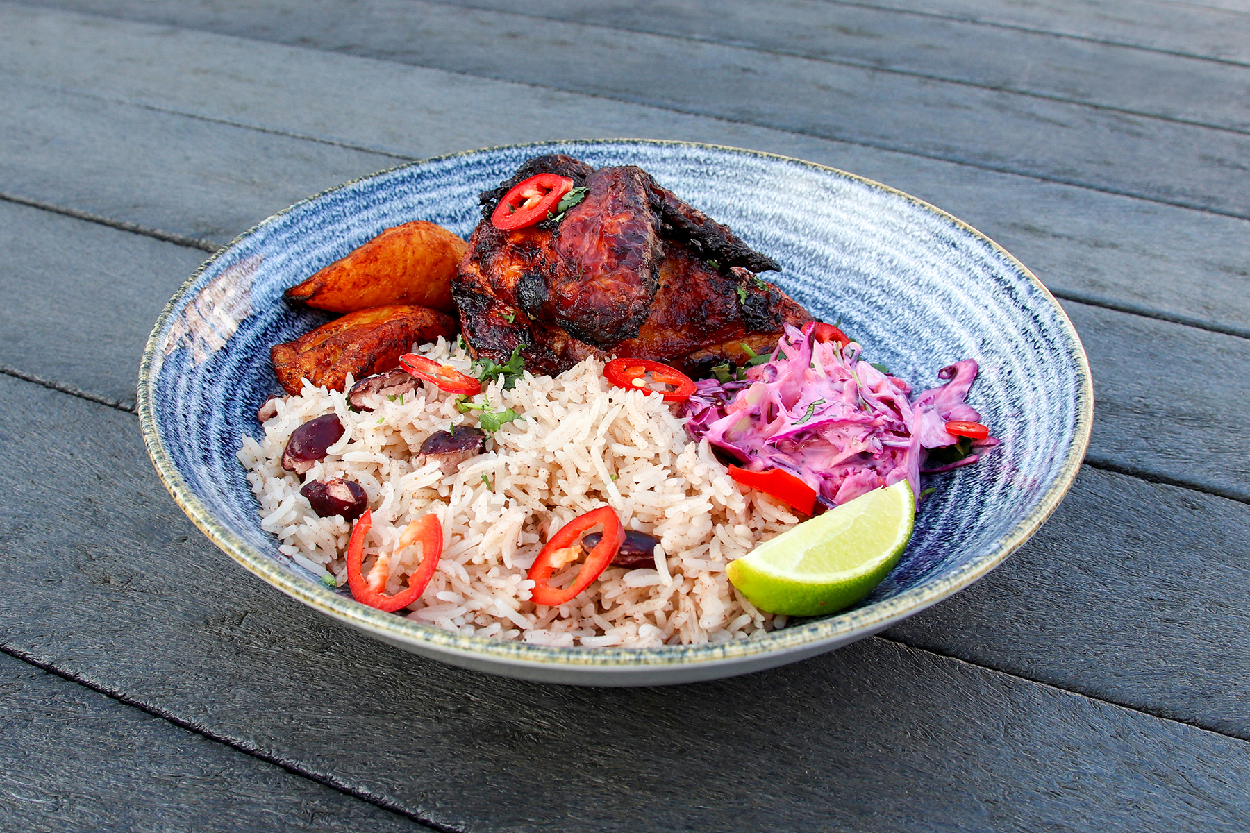 Jerk Chicken: a spicy quarter of chicken served with rice and peas, creamy coleslaw, and golden fried plantain