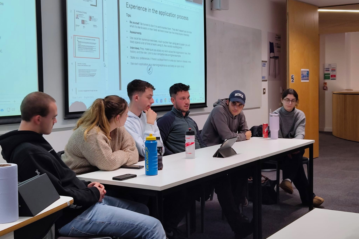 Six of the Economics Society members sat at a table at the front of the room, with a powerpoint presentation showing behind them