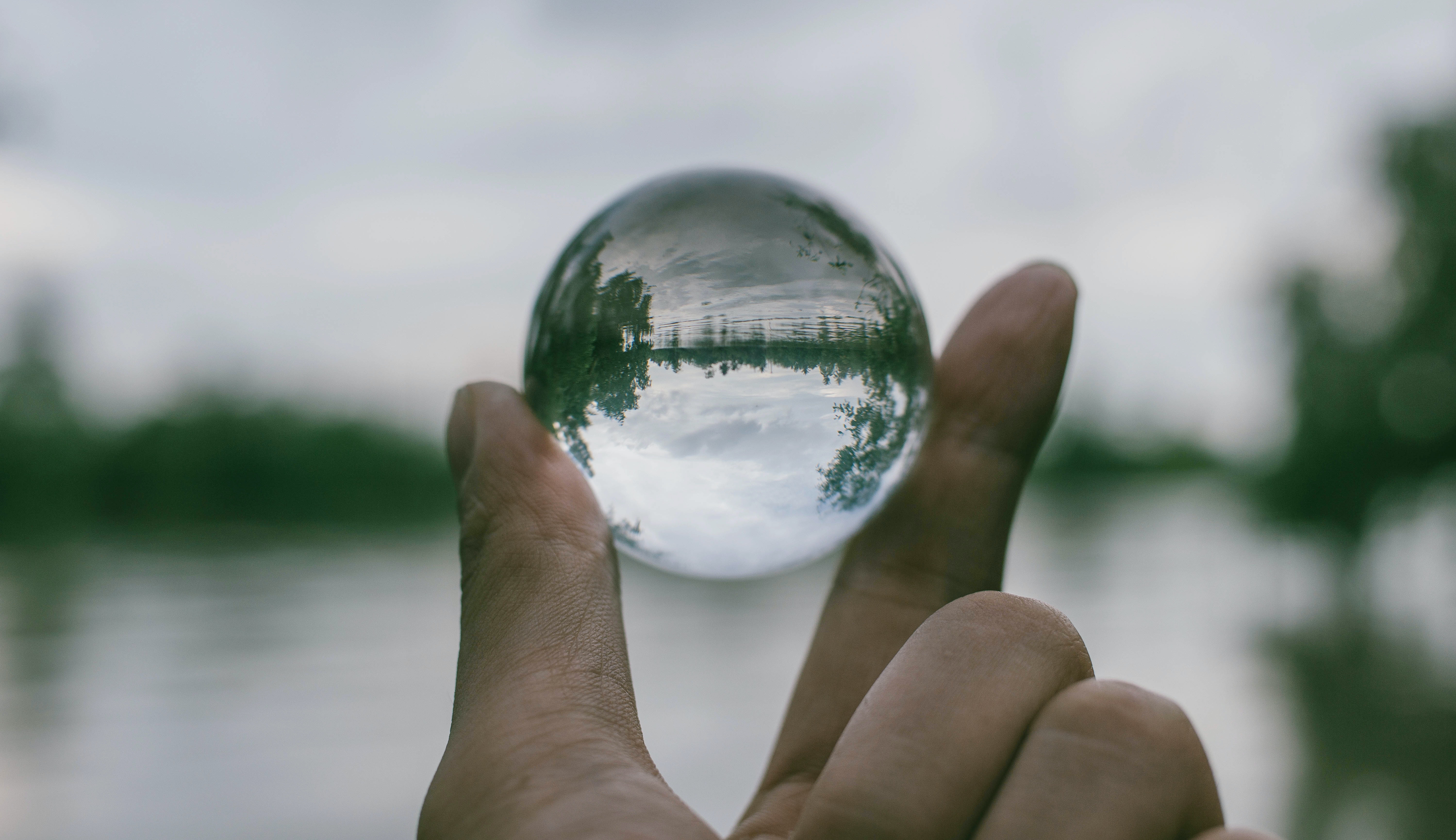 image of a hand holding transparent sphere through which the background scenery can be seen
