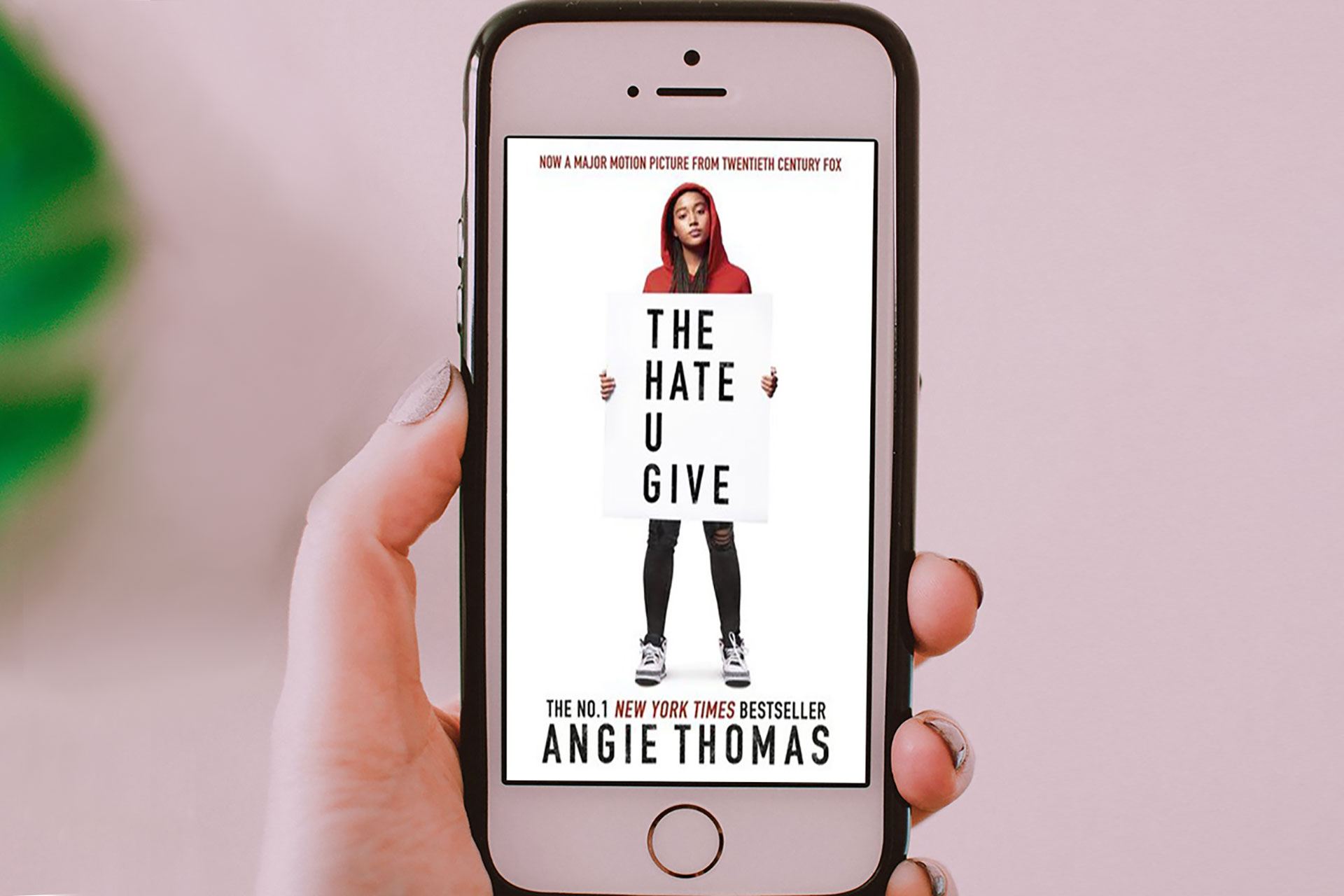 Hand holding mobile phone showing The Hate you Give book cover