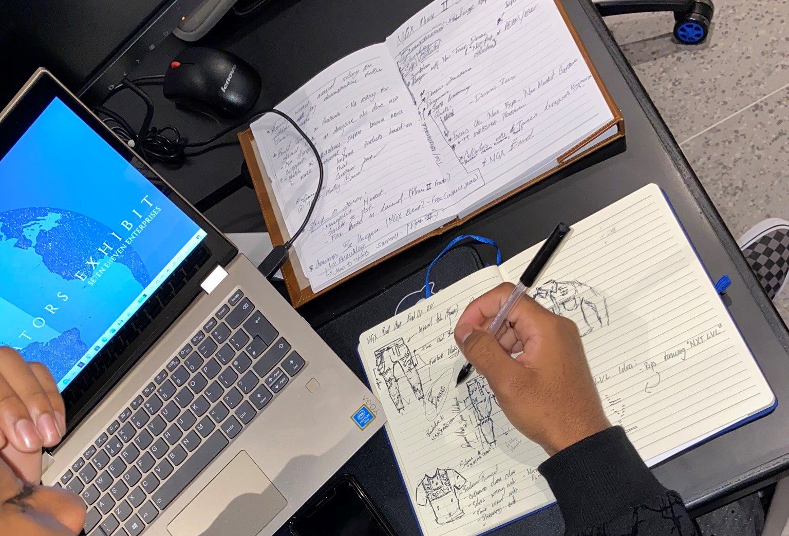 student designing on paper with a notebook and laptop on the desk