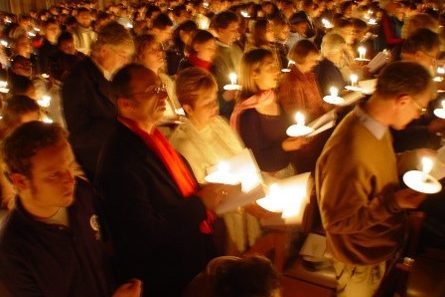A crowd of people singing and holiding candles in a carol service.