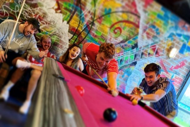 winning photo of pink pool table with friends and colourful wall in background
