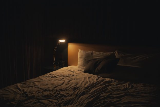 Bed in dark room with small side lamp on
