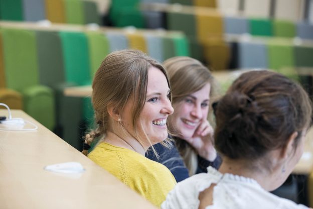 Three students smiling to each other in a lecture theatre