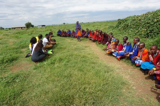 People from Massai village in Amboseli, Kenya sat on grass
