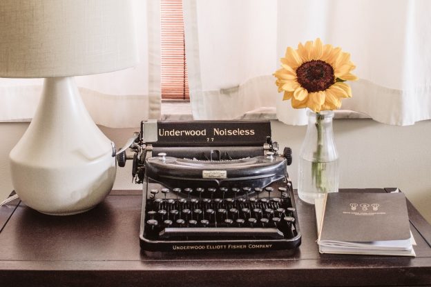 Typewriter with sunflower in vase next to it