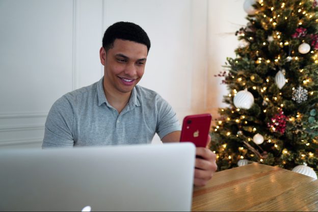 Man working on his laptop and iphone with Christmas tree in the background - Unsplash