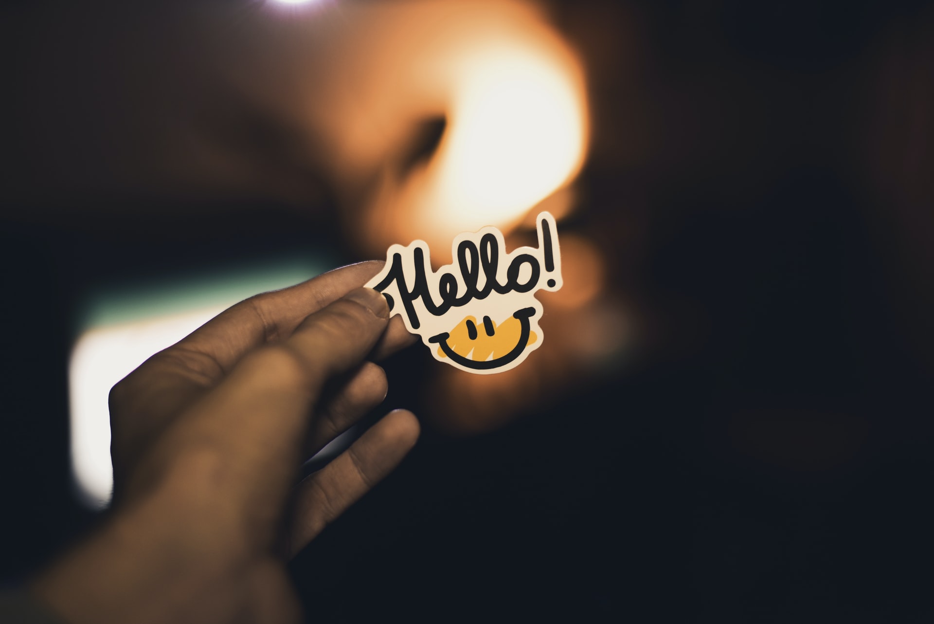 Hand holding "hello" sticker with smiley face