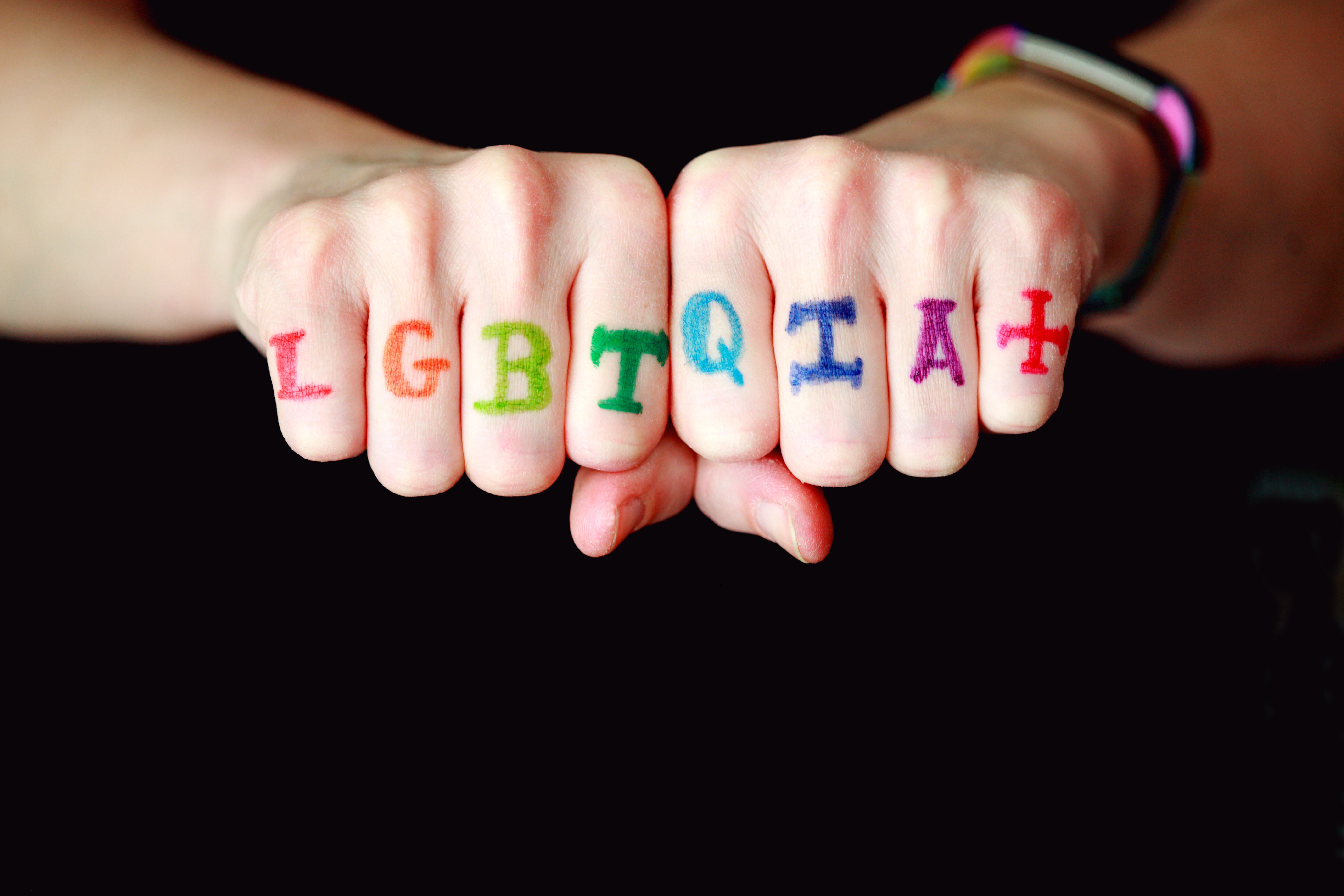 LGBTQIA+ letters written in the colours of the rainbow on closed fingers on hands pressed together