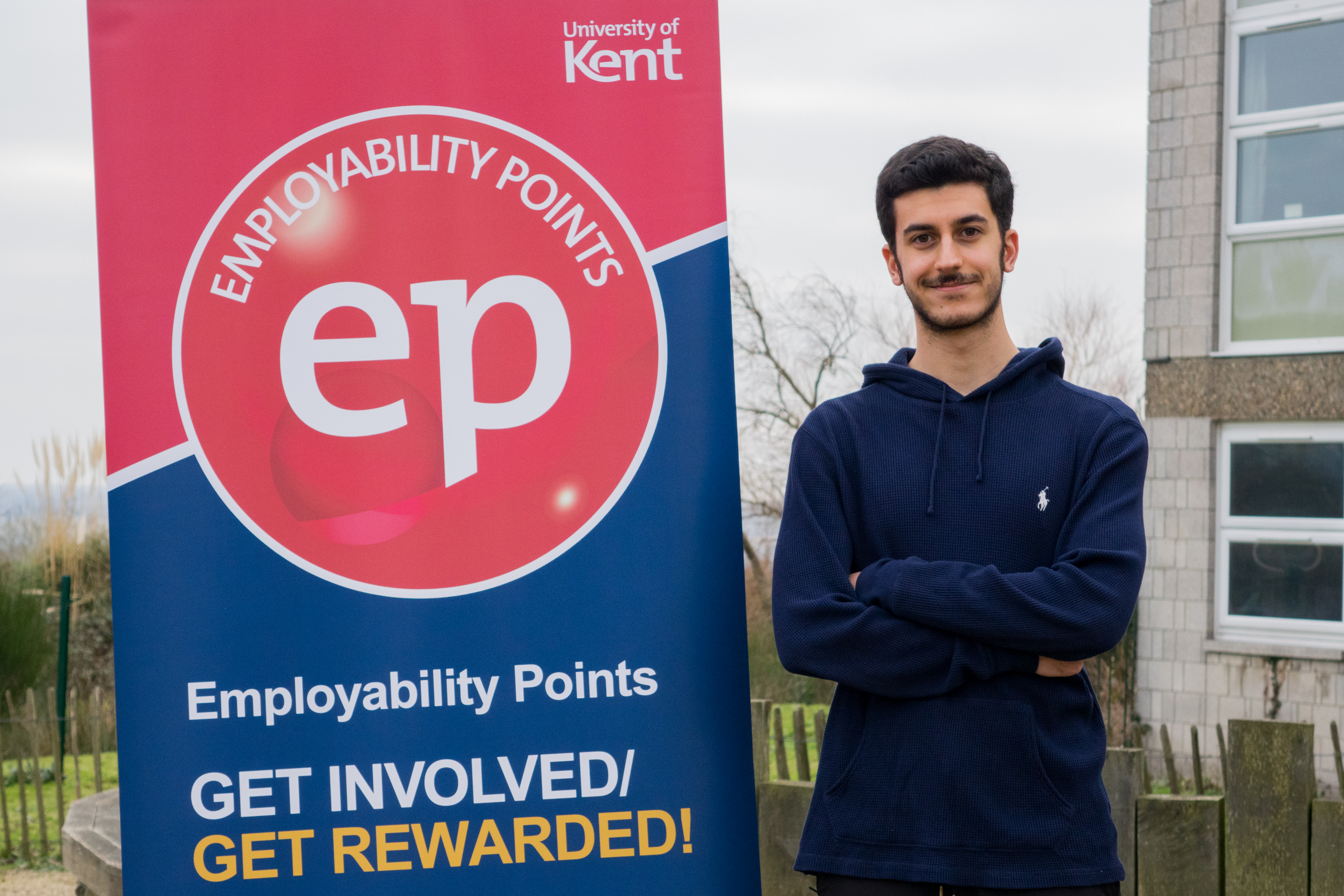 Student Sami standing next to Employability Points scheme banner