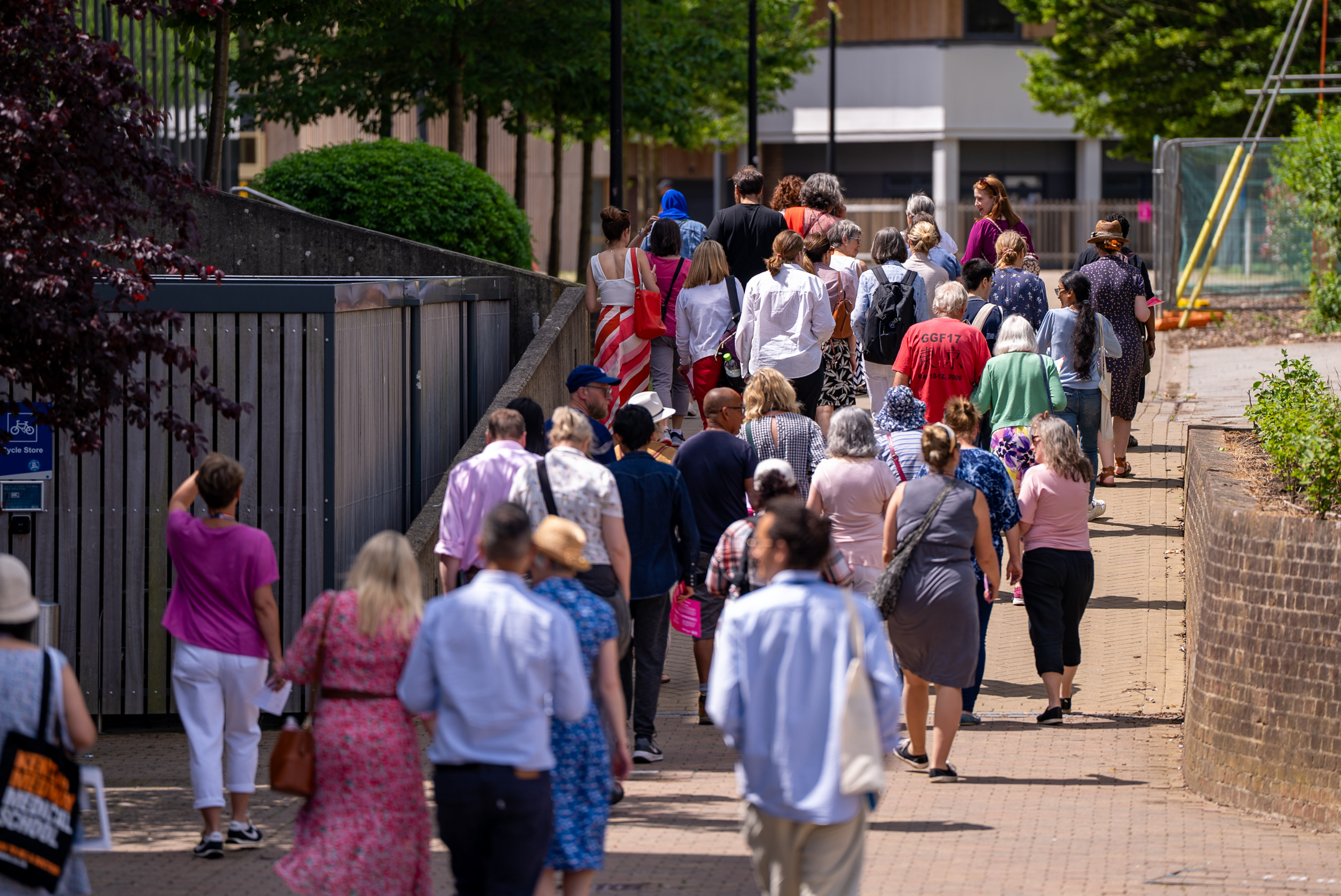 photograph of approximately 40 people walking away from the camera along a pathway, wearing a variety of colourful casual clothing