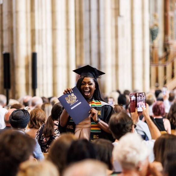 Black female student holding degree and smiling at graduation ceremony