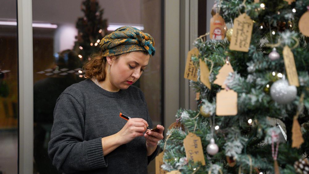 woman writing on a tag next to a decorated christmas tree