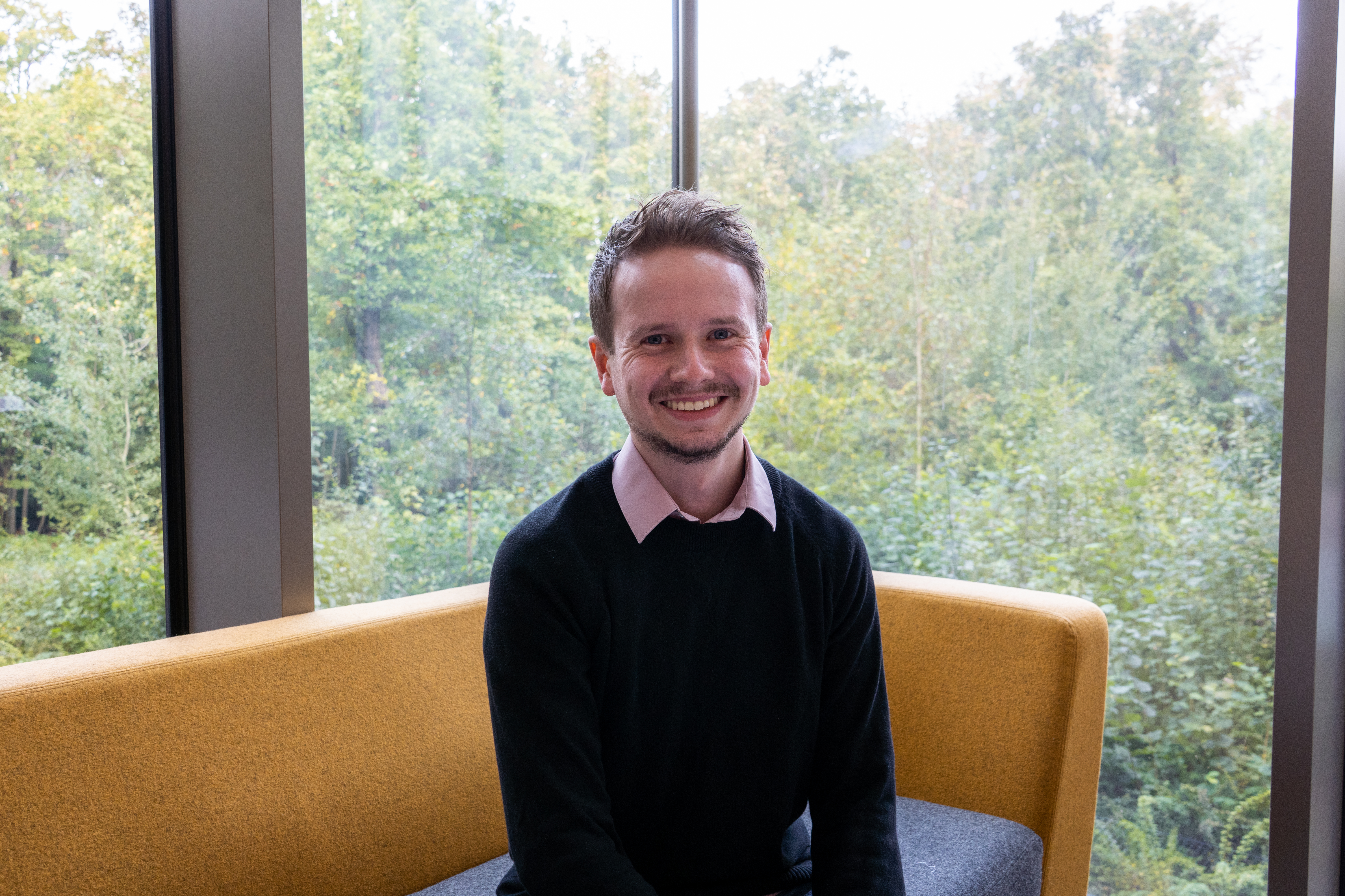 young caucasian male sitting on a yellow sofa, smiling at camera