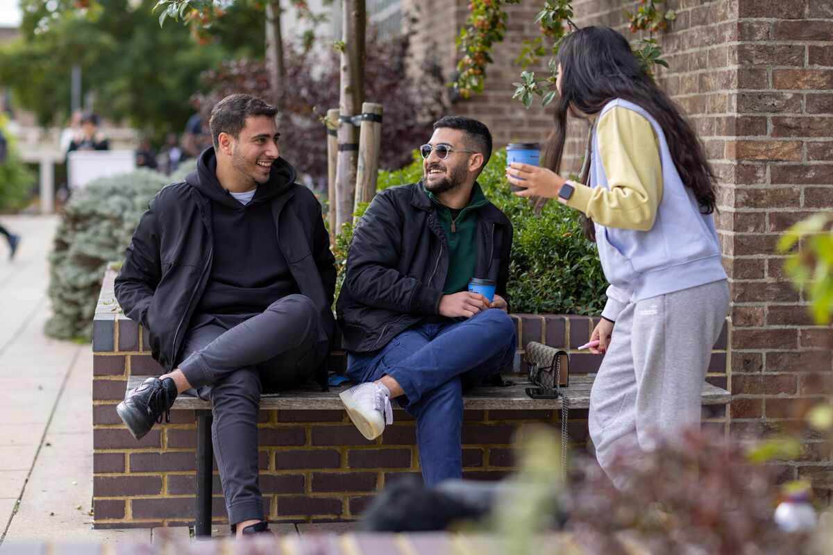 Students laughing enjoying takeaway coffee outside the library