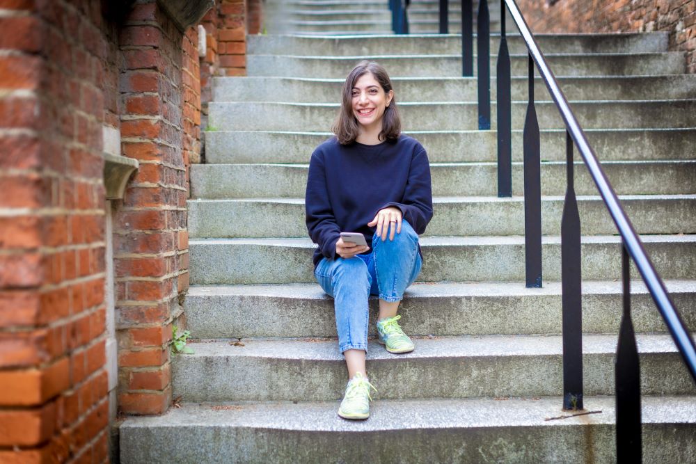 Student sat on steps smiling holding phone