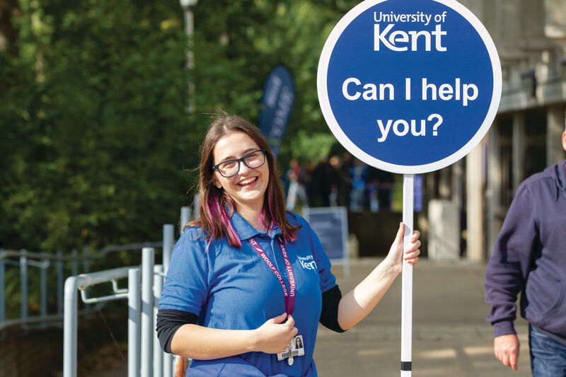 Student smiling holding sign that says "Can I help you?"