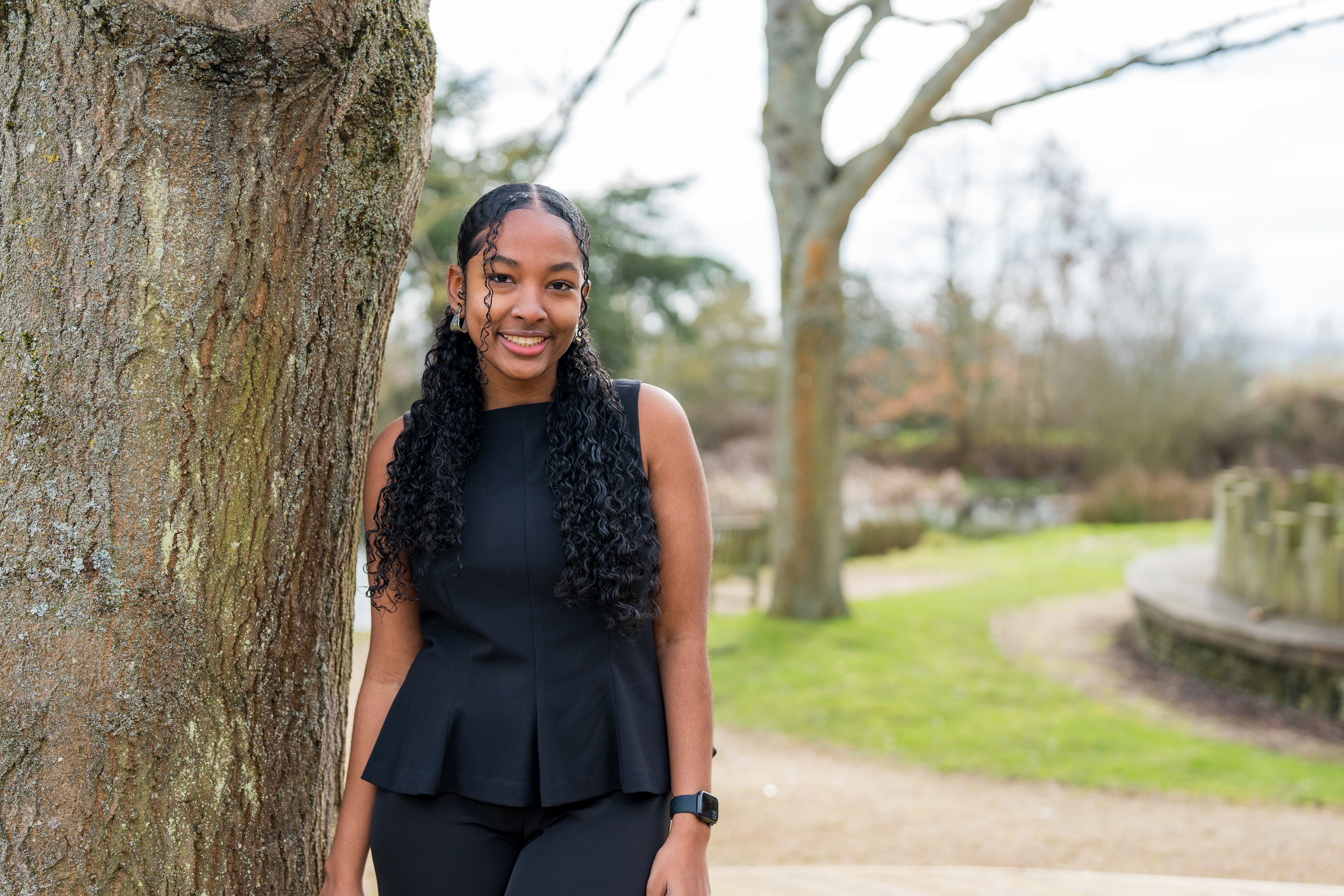 Student Kerriva smiling leaning by tree