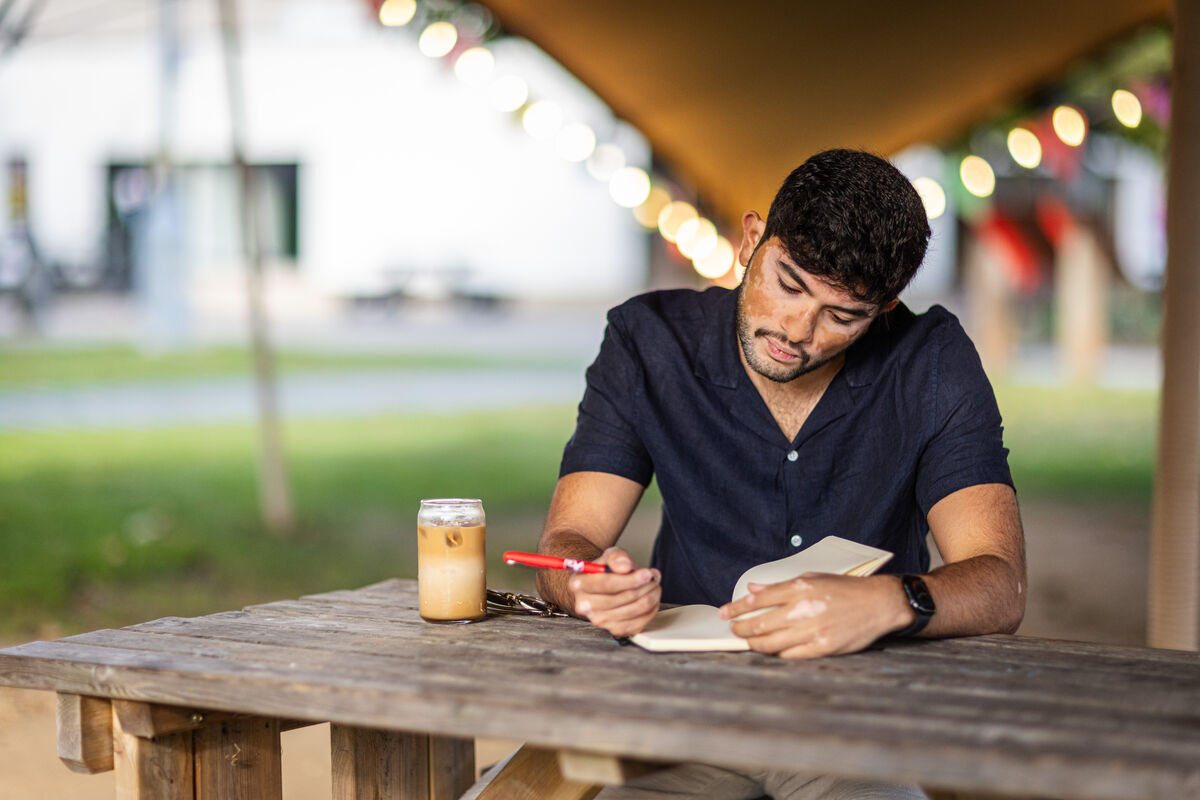 Student writing in notebook on bench outside