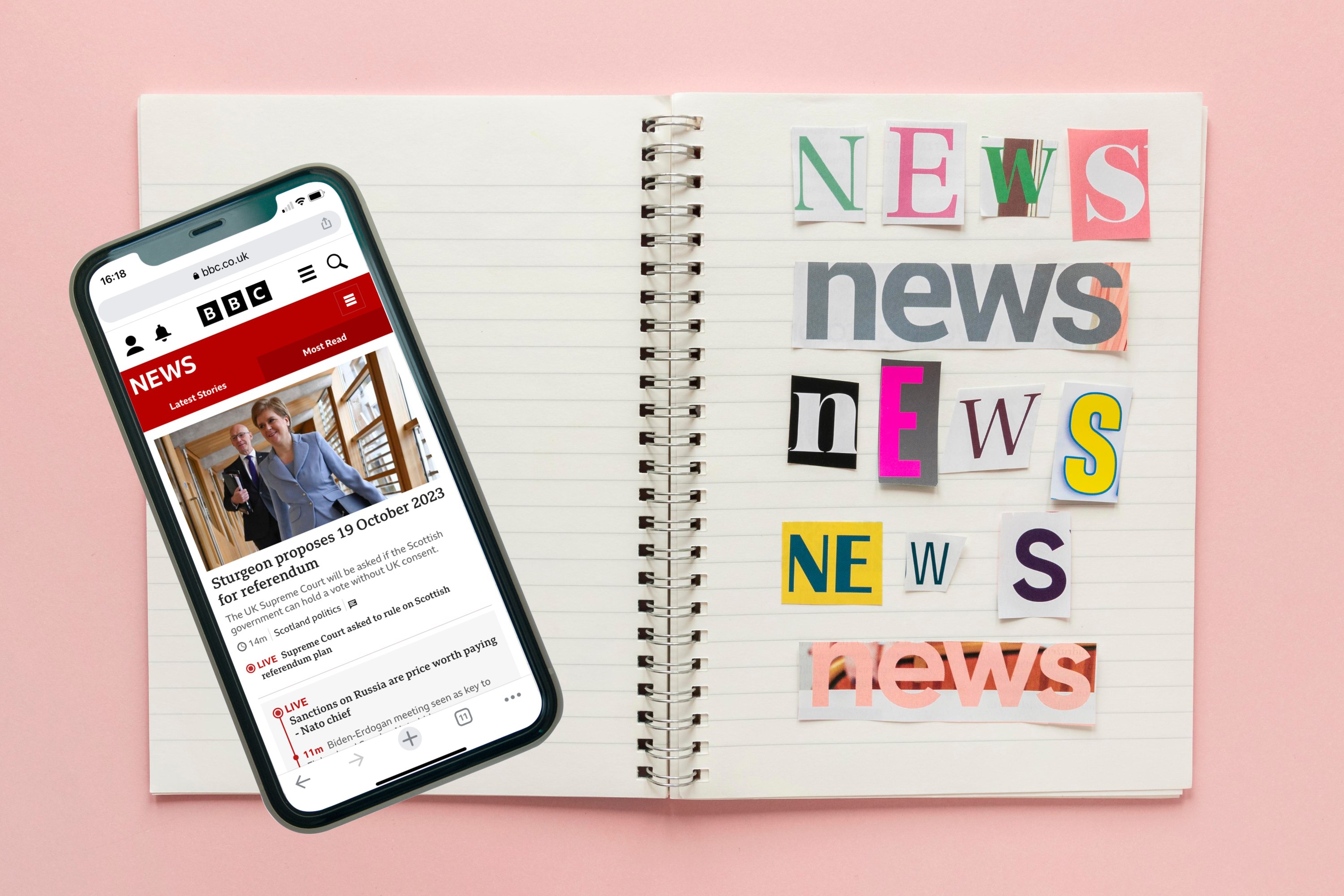 Notebook with cut and paste letters spelling 'News' with a smartphone resting on top showing the BBC News page.
